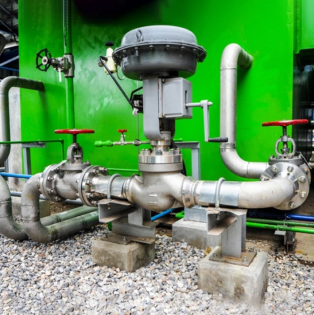 Válvula de control con actuador de membrana instalada sobre línea de acero inoxidable junto a un depósito verde